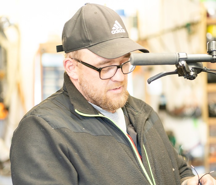 Ein Mann mit Baseballkappe und Brille arbeitet konzentriert an einem Fahrradlenker in einer Werkstatt.